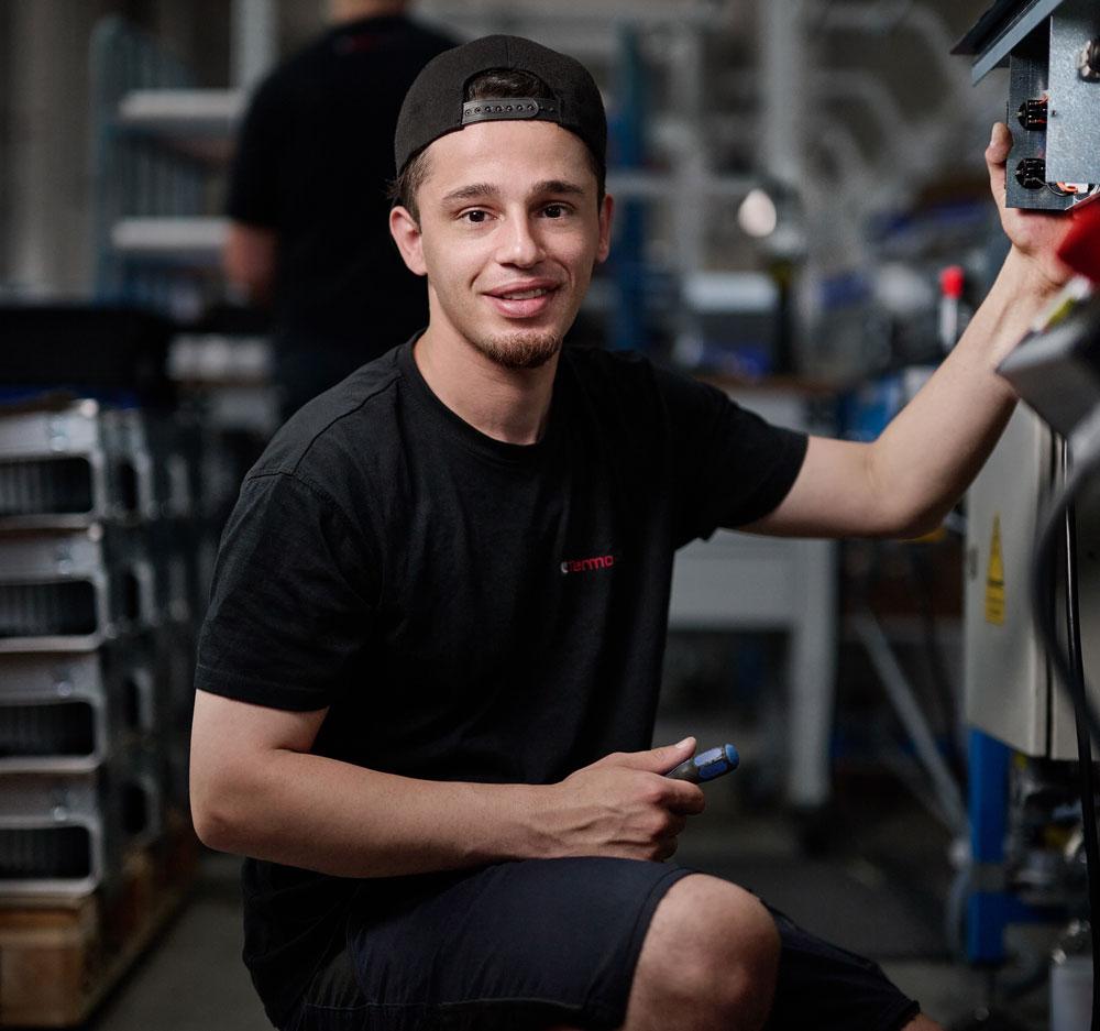 Ein junger Mann sitzt in einer Fabrik und bedient eine Maschine.