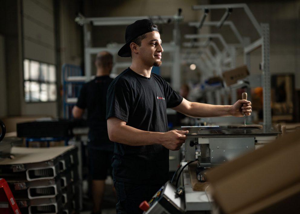 Ein Mann in schwarzem Shirt und Cap arbeitet an einer Maschine.